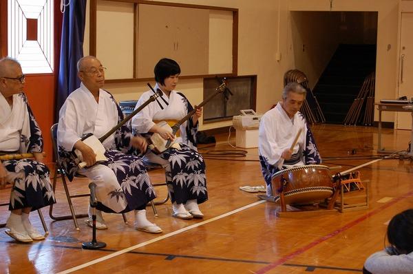 浴衣を着た人たちが子供達の前で締太鼓、三味線を弾ている写真